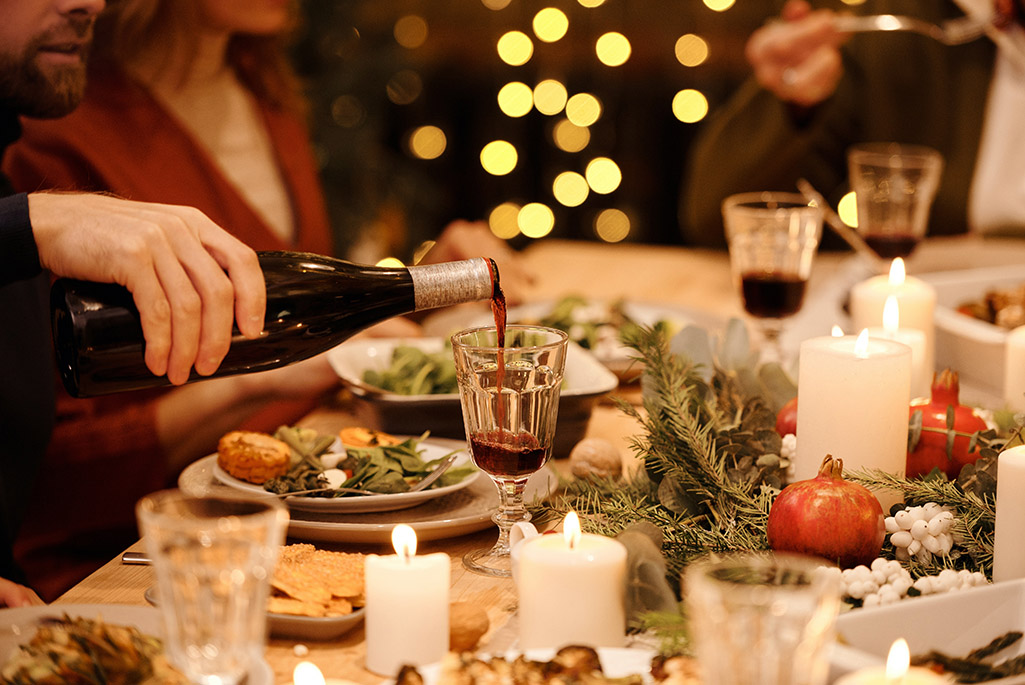 Foto på ett julbord fyllt med mat. På fotot syns också en hand som häller upp vin i ett glas.