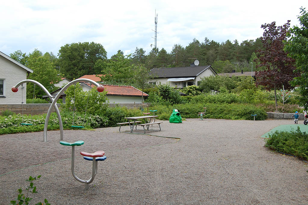 Lekplats med lekställningar omgivna av träd.