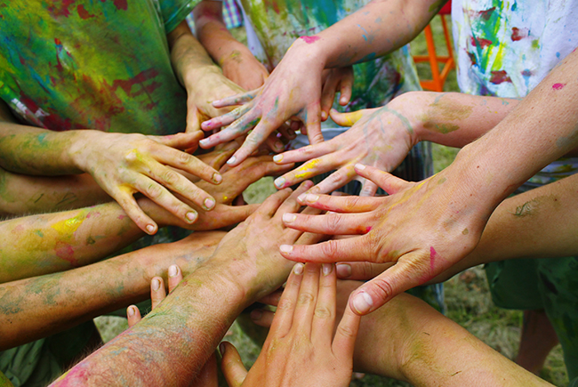 Flera personer sträcker in sina händer målade med färger in i mot mitten och bildar en cirkel.