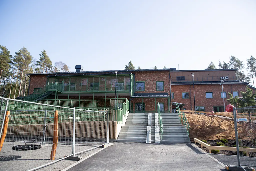 Förskolebyggnad i två våningar i tegel. I förgrunden lekställning med bin.