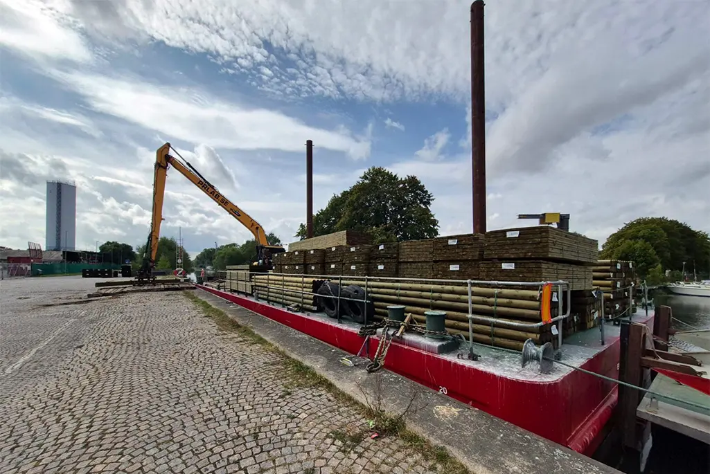 Röd pråm lastar virke vid hamn