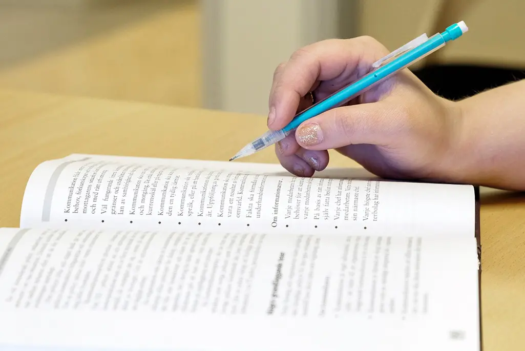 Hand håller i en penna och anteckning i en bok med text
