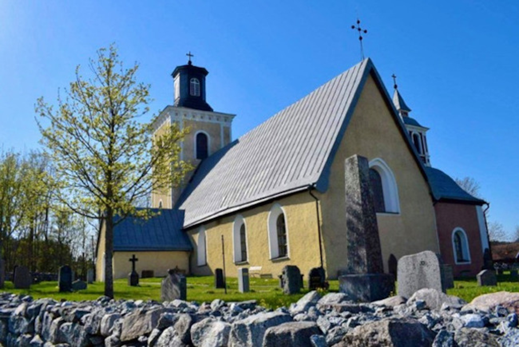 Bild på Vallby kyrka. En gul stenbyggnad.