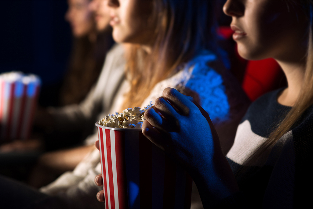 Foto på flera ungdomar som sitter i en biosalong och äter popcorn.
