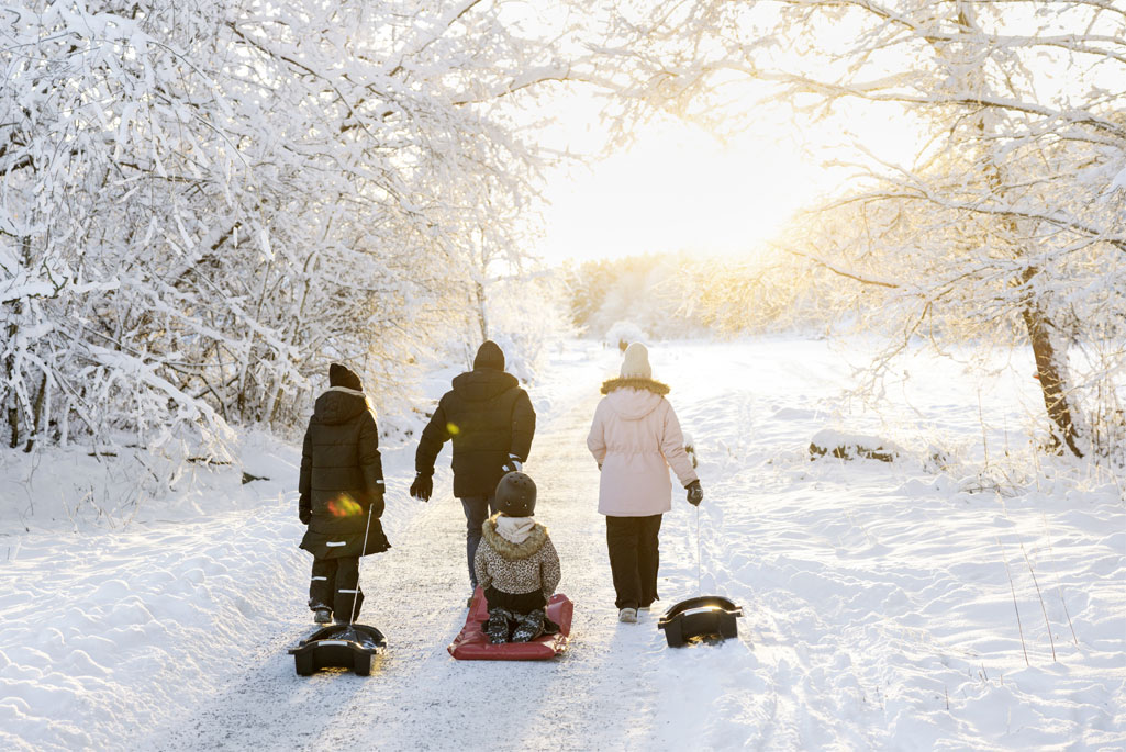 En familj med barn som är på väg att åka pulka utomhus i snön.