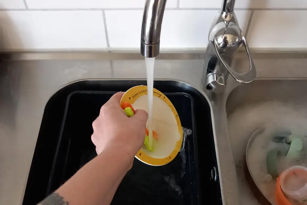 Diskho med svart balja och rinnande vatten från kökskran.